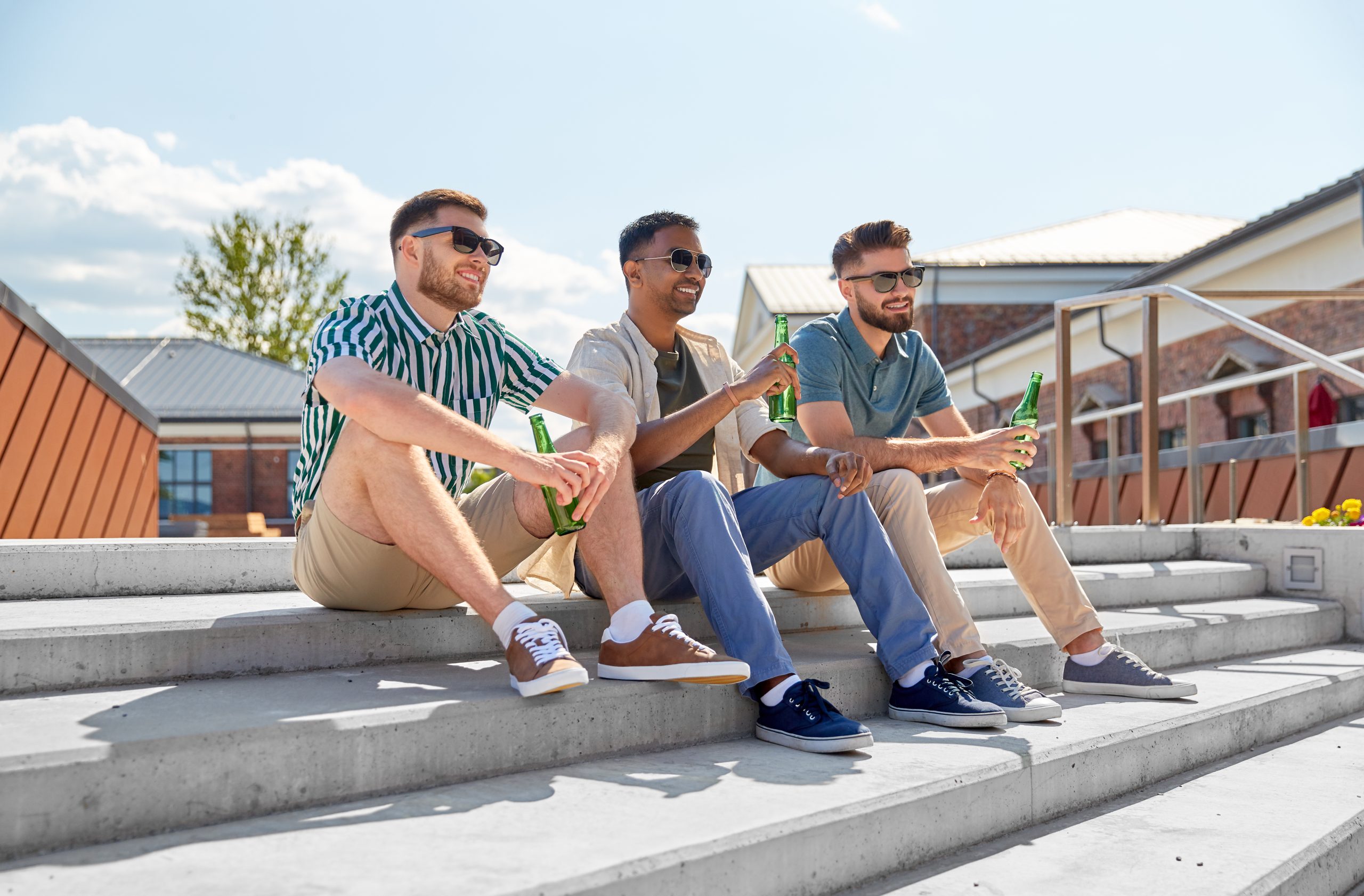 leisure, male friendship and people concept - happy men or friends drinking beer and talking on street in summer